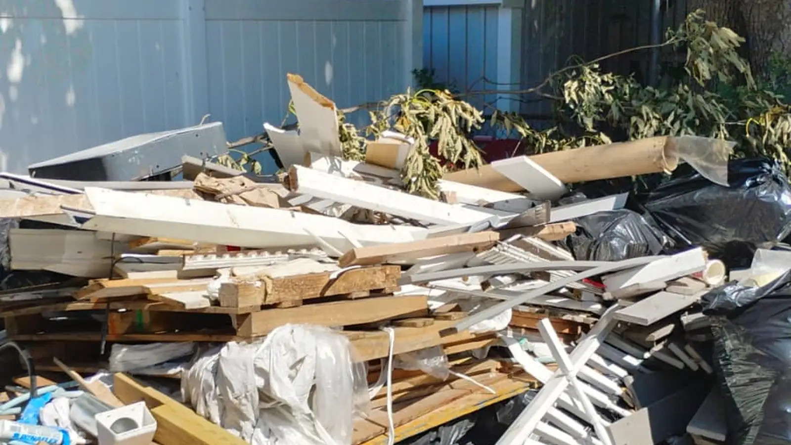 Renovation lumber, old trim and bags piled in a backyard before junk removal