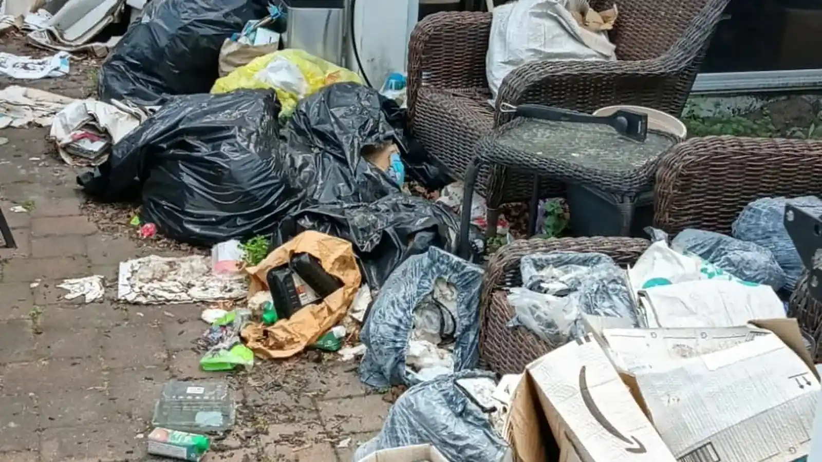 Trash bags, boxes and worn wicker chairs covering a patio before a cleanout