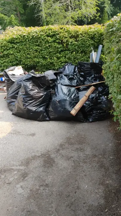 Driveway corner piled with trash bags and lumber before a junk removal job