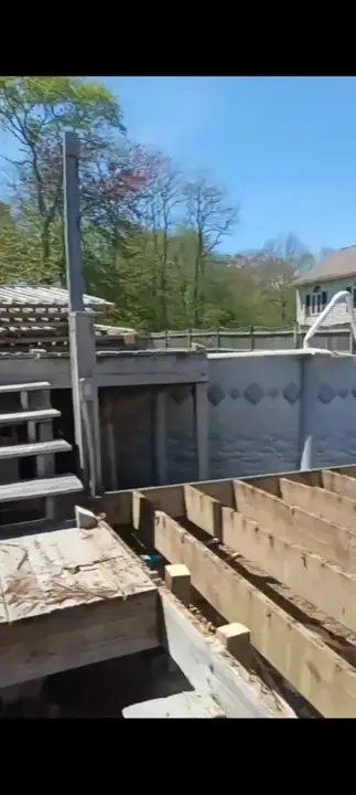 Wooden pool deck boards and framing being taken apart beside an above-ground pool